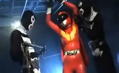 Sexy Super Hero in orange latex is strung up and tortured b